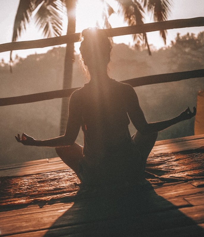 Woman meditating in cross-legged pose on a wooden deck at golden sunset
